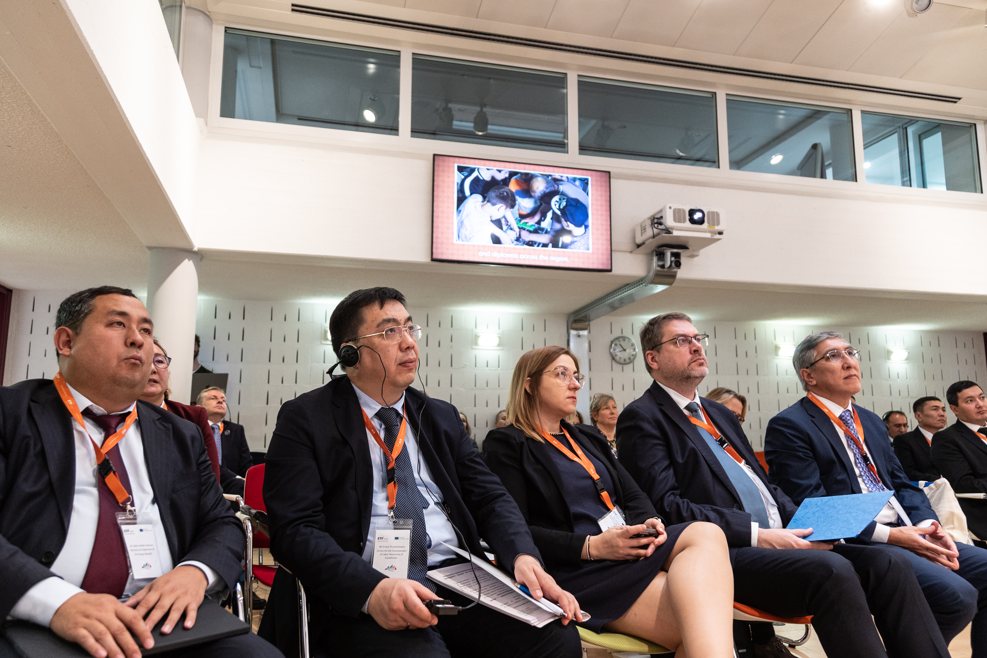 Photo of events room featuring men and women in suits sitting and watching a presentation