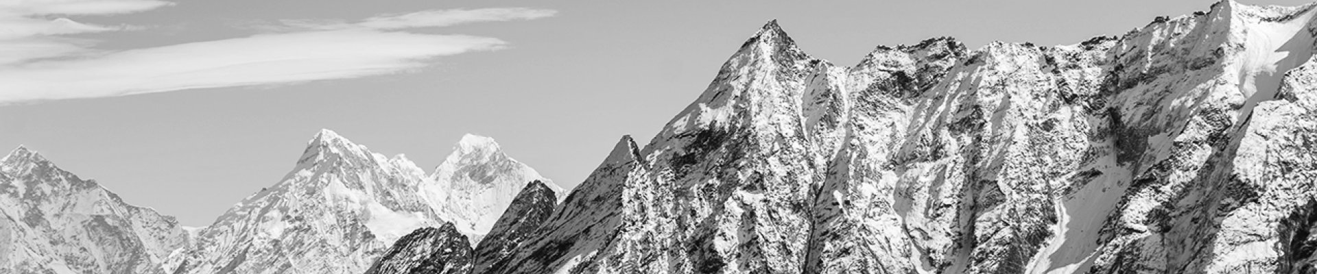 Black and white photo of a mountain range with snow, against a clear sky.