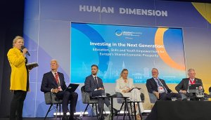Dressed in a yellow blazer and situated to the left of the frame, ETF Director Pilvi Torsti addresses a conference room, microphone in hand, with other panellists sitting to her right watching her deliver her address