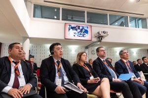 Photo of events room featuring men and women in suits sitting and watching a presentation