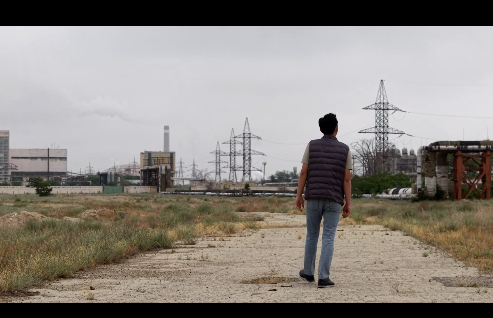 A boy walking towards an old  fossil fuel industrial power plant area in Kazakhstan