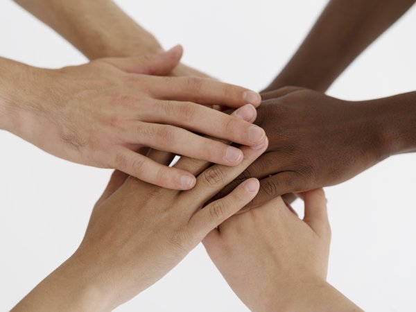 Six multi-racial hands pile in on top of each other, against a white background